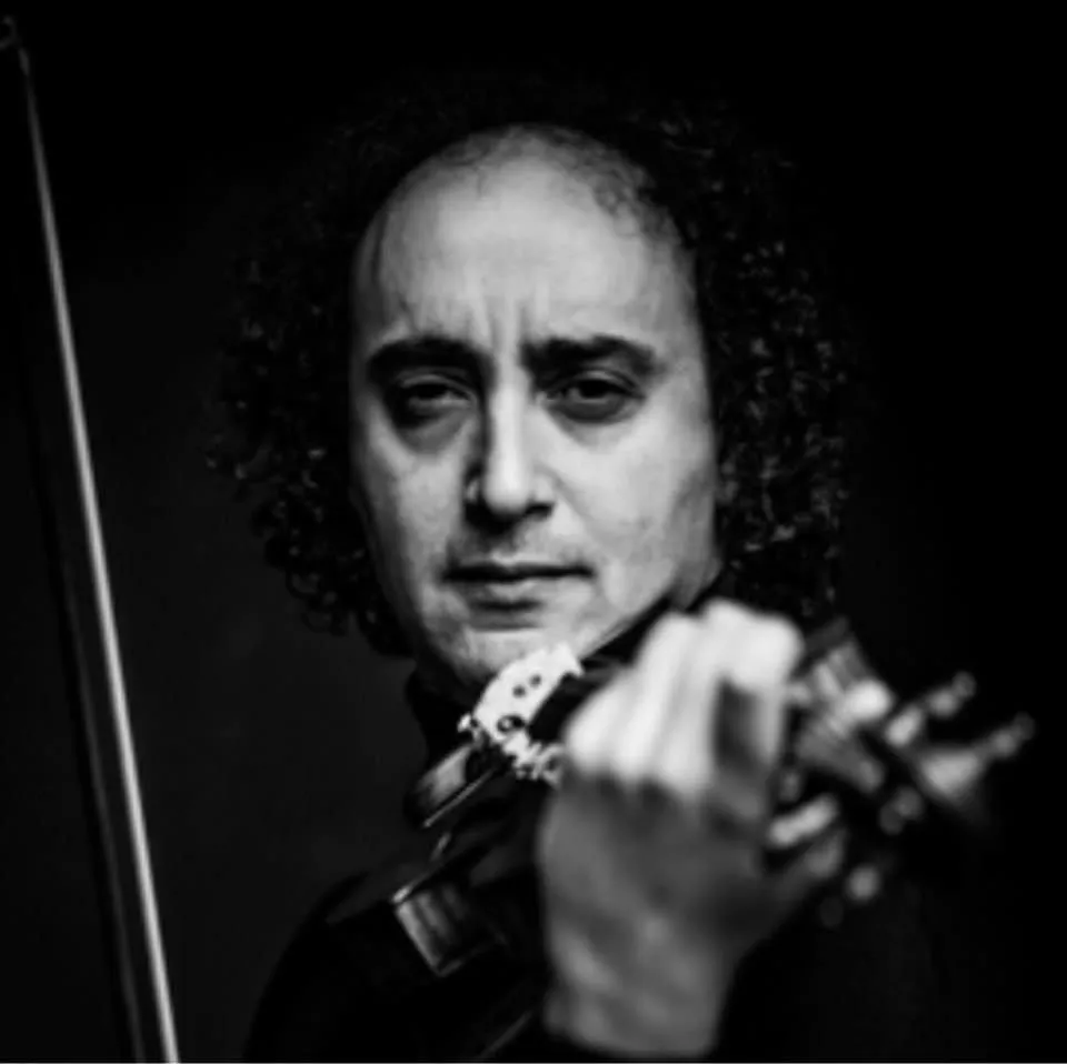 Black-and-white close-up of Mario Hossen looking over the scroll of his violin, the pegbox in sharp focus and his face softly out of focus behind it