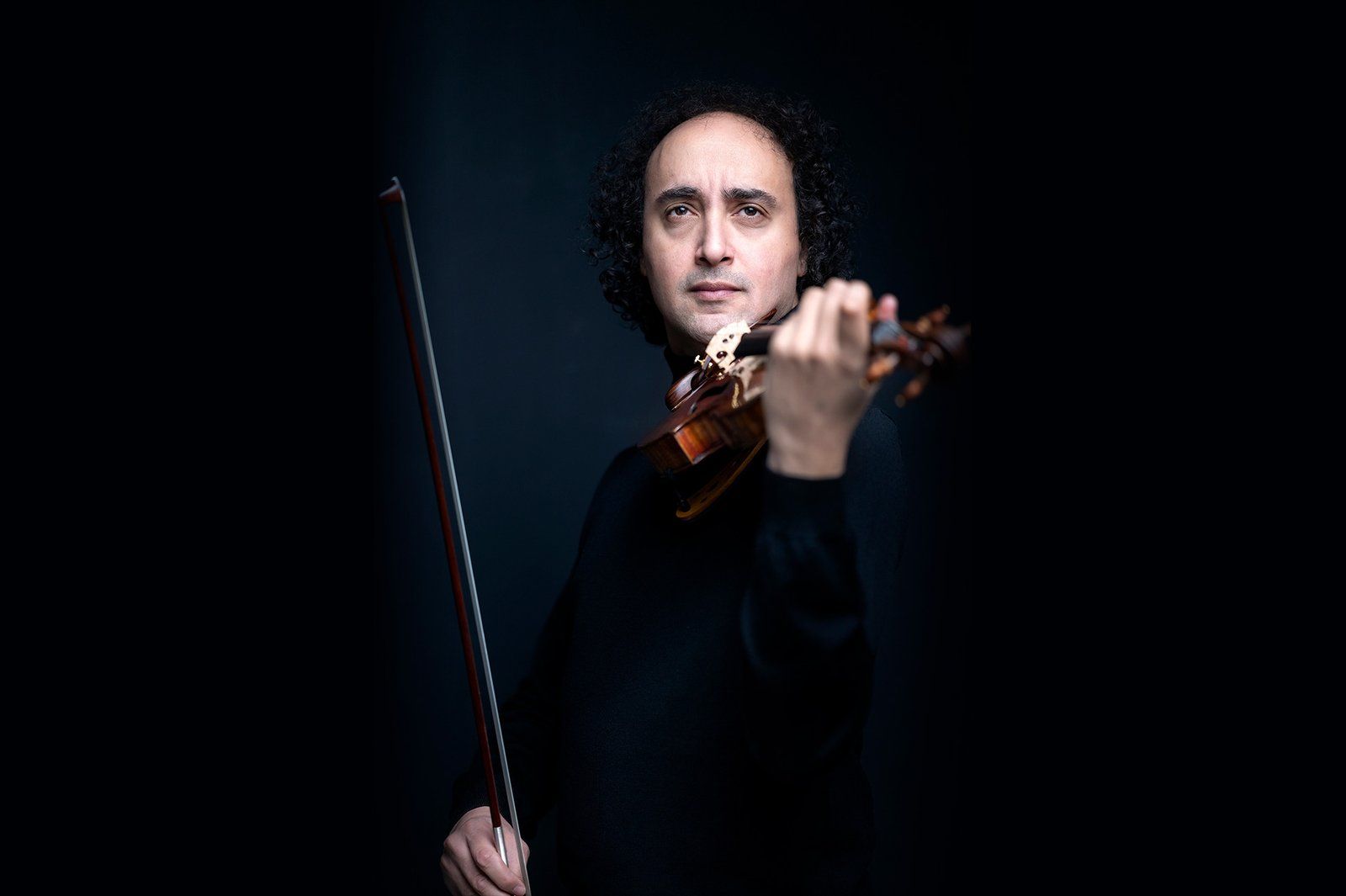 Close-up of Mario Hossen playing the violin, sharp focus on his face and the instrument with the bow softly blurred in the foreground